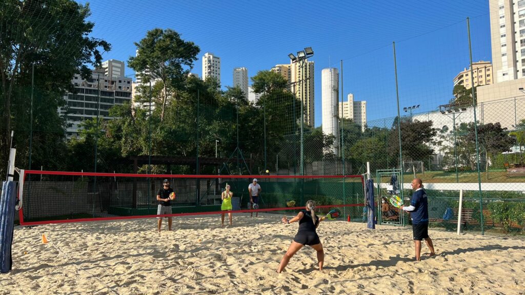 Quadra de beach tennis em condomínio: quatro pessoas durante jogo com professor