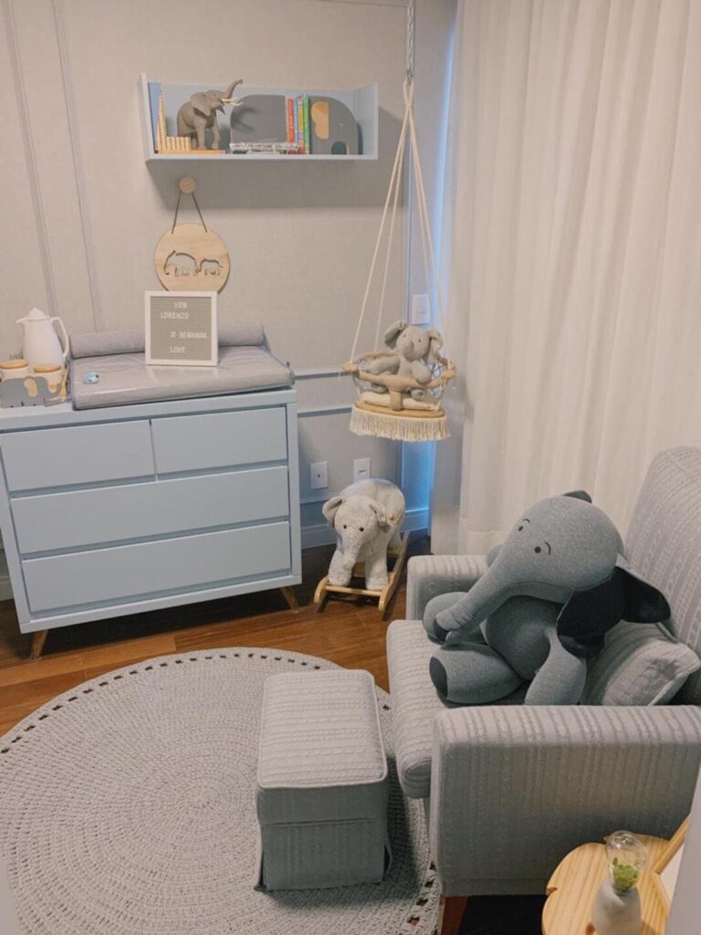 Tapete de crochê cinza, redondo, no quarto do bebê, segue a mesma cor da poltrona, cinza, e não contrasta com as paredes claras e a cômoda azul claro
