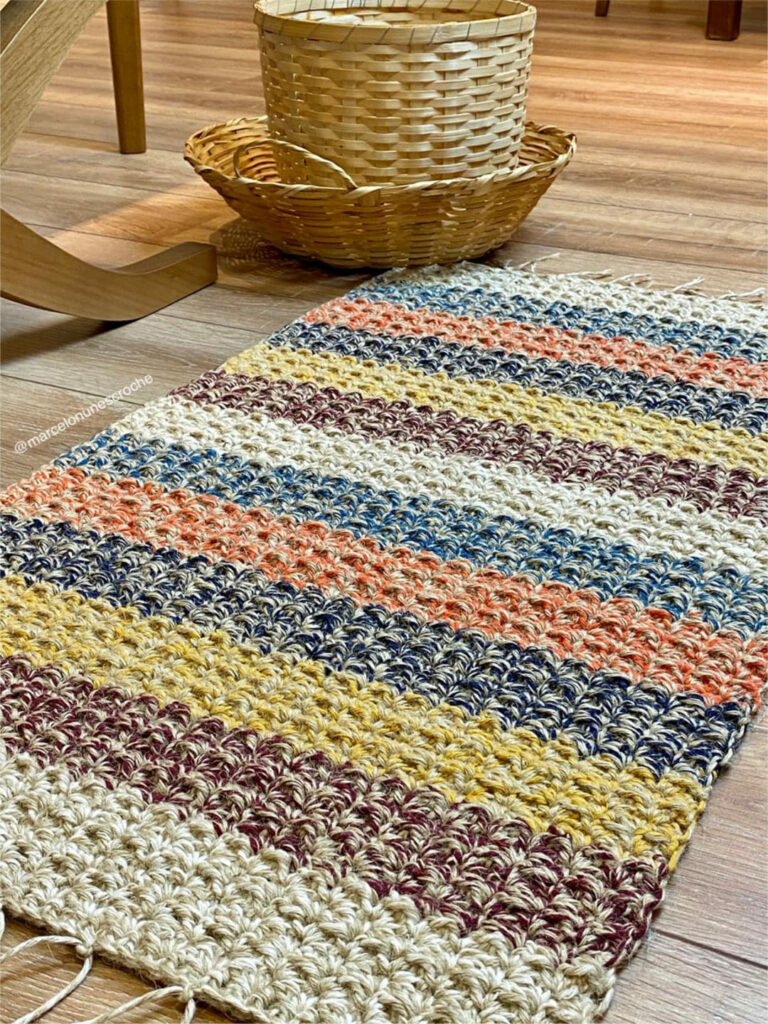 Tapete de crochê colorido, com listras de cores cru, marrom, amarelo, azul e laranja, todos mescla com branco, retangular, feito de fibra de juta natural