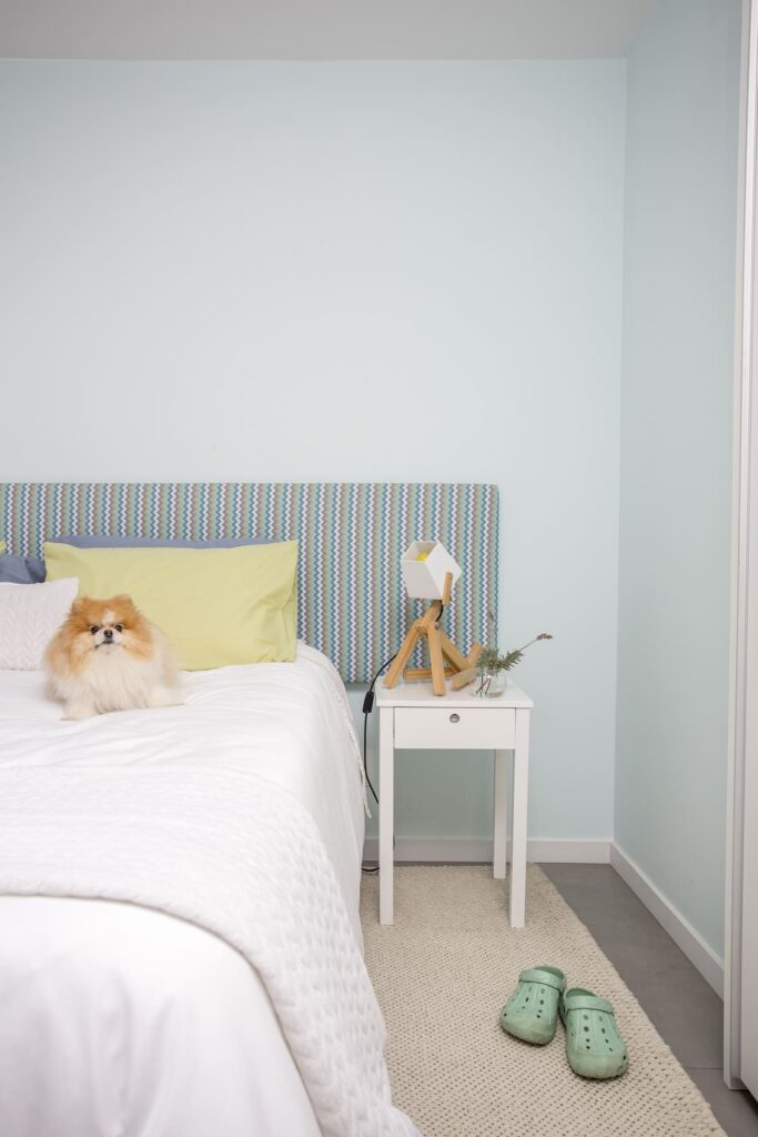 Tapete de crochê cru, no quarto, ao lado da cama. O tom claro combina com os lençóis brancos e paredes claras