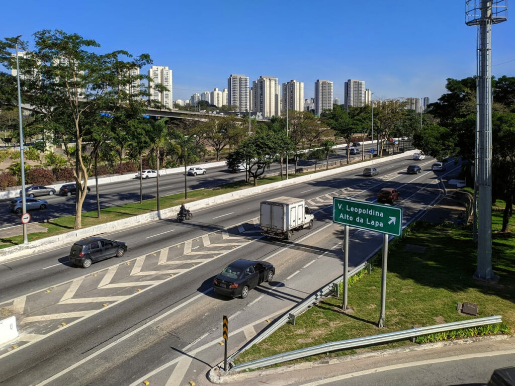 Imagem mostra a marginal Tietê e placa de acesso que diz V. Leopoldina e Alto da Lapa, com prédios e rio ao fundo