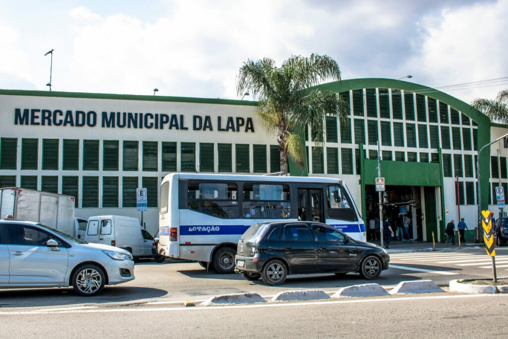Mercado da Lapa com carros e vans passando em frente, com clientes saindo e entrando do local