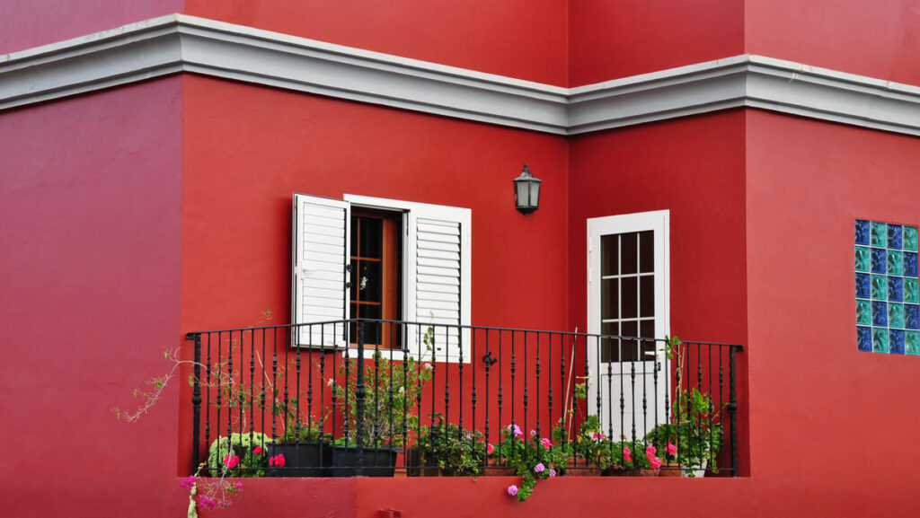 Fachada de casa pintada de vermelho, com janelas e portas em branco e uma pequena varanda com vasos de flores
