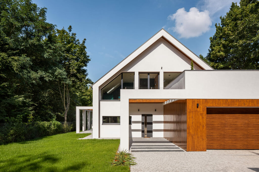 Fachada de casa sobrado branco com garagem em destaque, com acabamento em madeira, e varanda e quintal na lateral