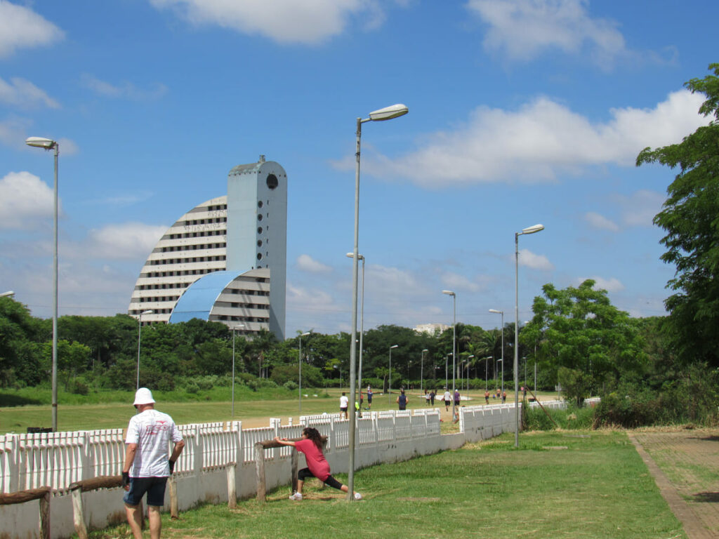 Pessoas fazem atividade física no Parque da Vila Guilherme, conhecido como Parque do Trote, em meio a arvores com prédio ao fundo