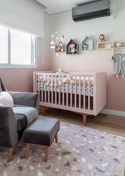 Quarto de bebê menina com parede pintada em degradê de rosa, berço rosa claro, bonecas nas paredes e poltrona cinza