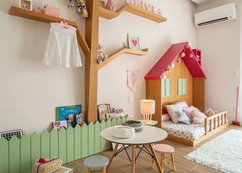 Quarto de bebê montessoriano com cama com desenho de casa, telhado rosa, estantes em forma degalhos de árvore e brinquedos
