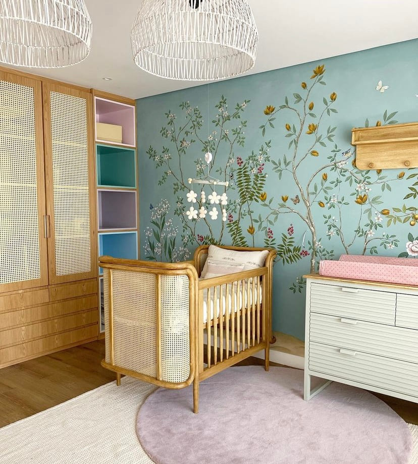 Quarto de bebê com papel de parede azul com desenhos florais, e móveis e berço em madeira com tela branca