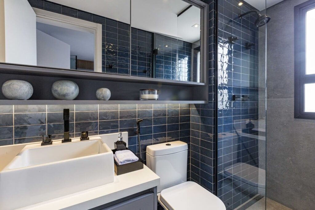 Decoração de banheiro pequeno com azulejos escuros, armário com portas revestidas de espelho e louças brancas