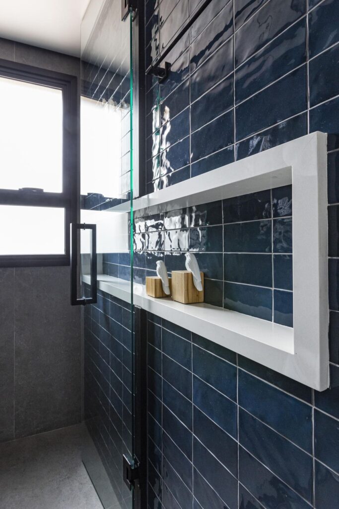 Detalhe de decoração de banheiro mostra azulejos escuros e nicho que se estende do chuveiro para o lado de fora