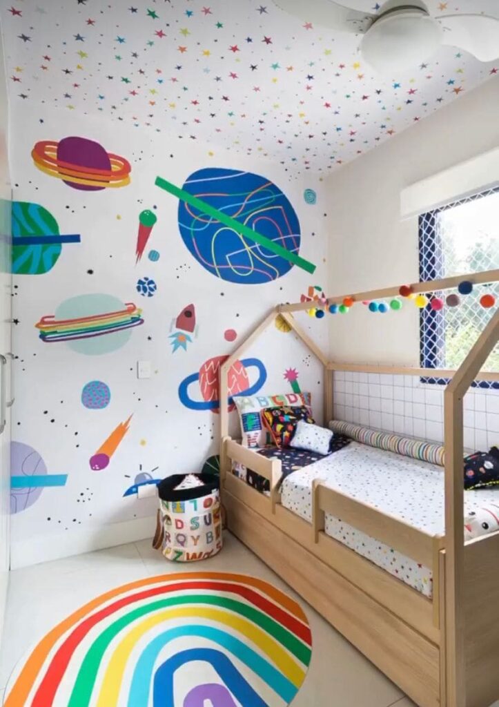 Decoração quarto menino com tema espacial com papel de parede com imagem de estrelas, planetas e foguetes, e cama em madeira