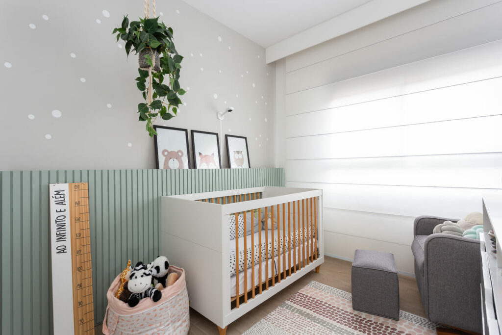 Decoração quarto bebê menino com persiana branca, que ocupa toda a parede. Poltrona em cinza, parede em verde e cinza, com quadros e planta de decoração
