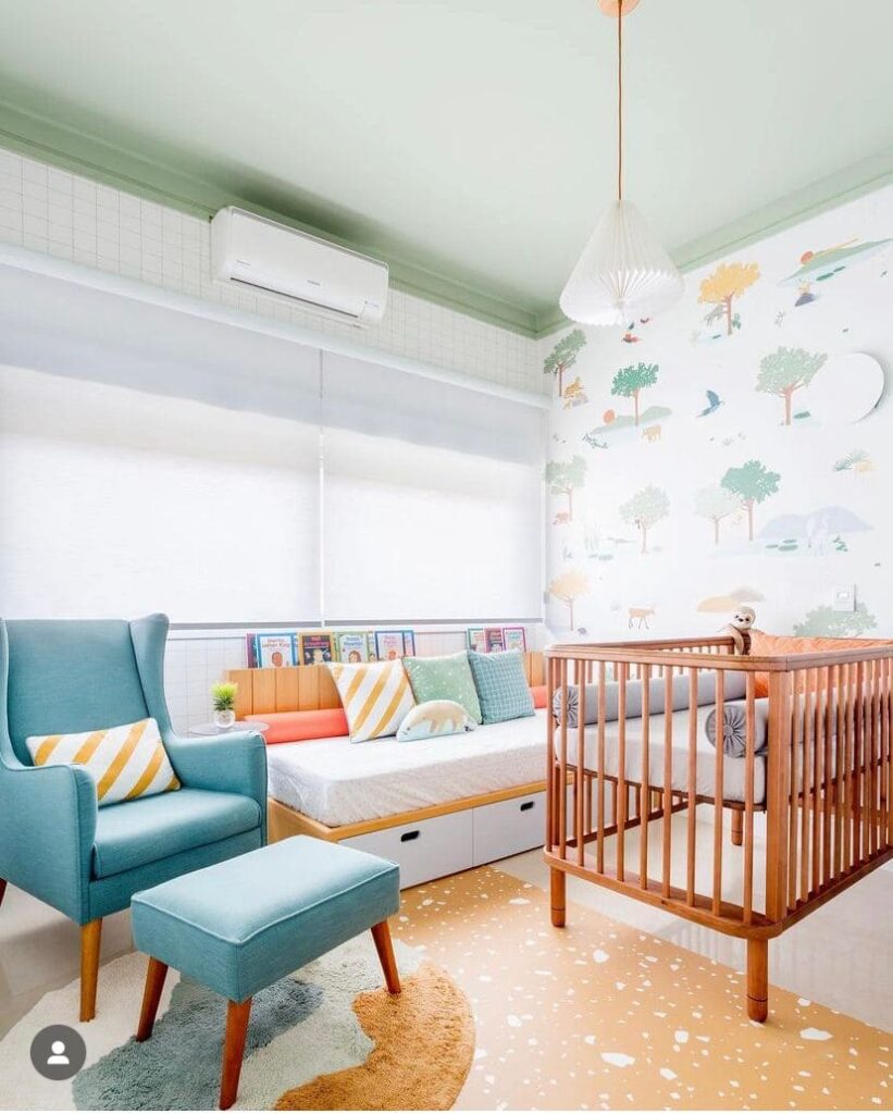 Decoração quarto bebê menino com persiana branca, papel de parede com desenhos, berço em madeira marrom, sofa-cama em tons claros e poltrona azul
