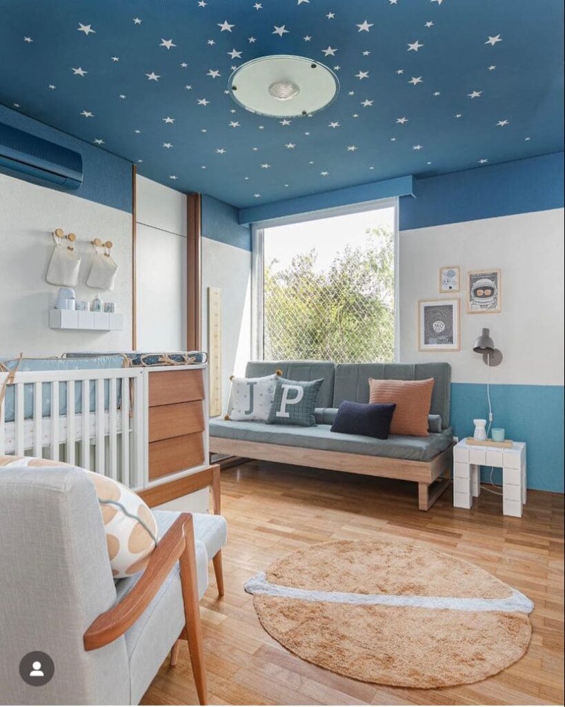 Decoração quarto bebê menino com teto em azul com estrelas brancas, paredes em dois tons de azul e branco, sofá cinza claro e berço branco