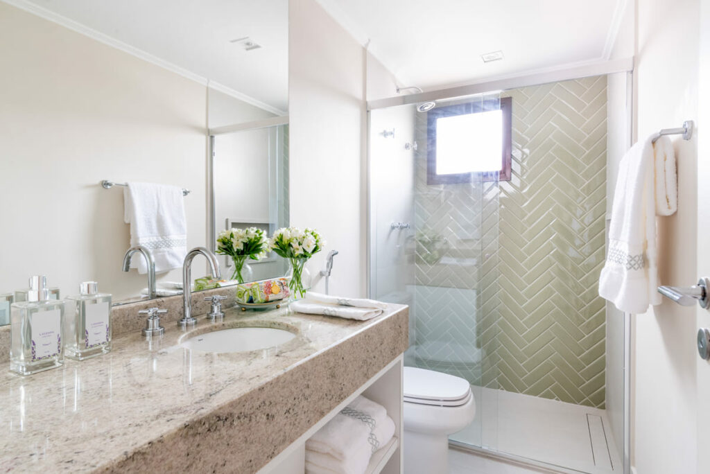 Banheiro em cores claras, com bancada de mármore em marrom claro. O ralo oculto linear perto da parede oposta à do chuveiro