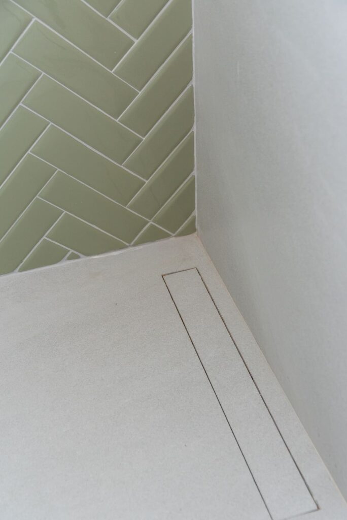 No destaque, ralo oculto linear dentro de box de banheiro. Piso branco e parede com porcelanato verde acinzentado
