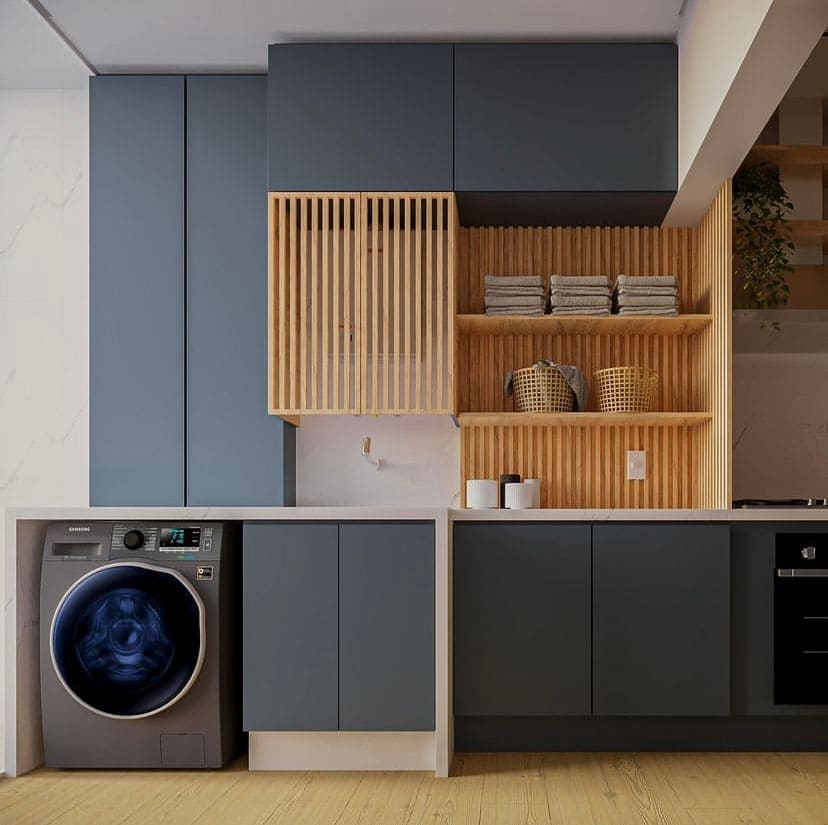Painel ripado em madeira clara divide lavanderia e cozinha, ambas com armários em azul escuro