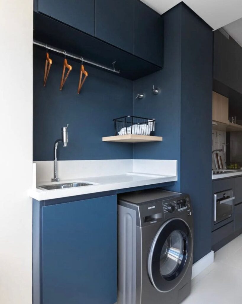 Cozinha e lavanderia divididas por parede com o mesmo tom de azul da marcenaria dos móveis da cozinha e da lavanderia. 