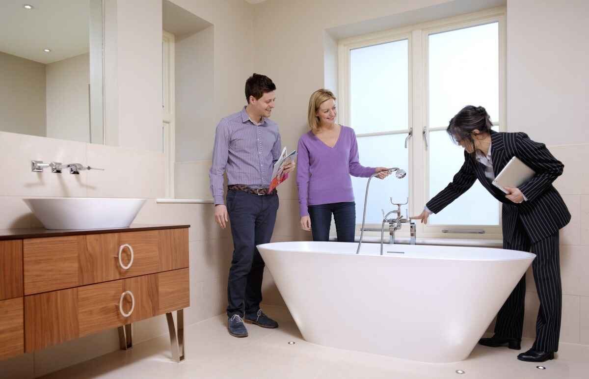 Corretora mostrando o banheiro para um casal, possíveis compradores do imóvel